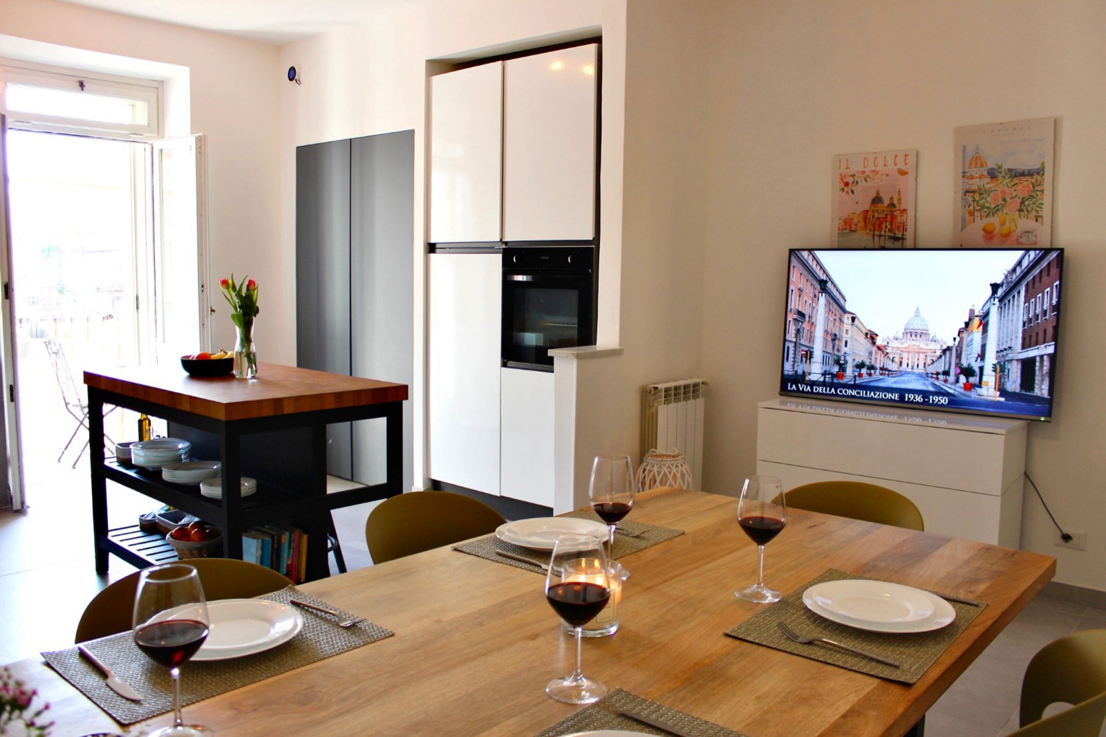 Dining table set for dinner, with the kitchen and balcony doors behind