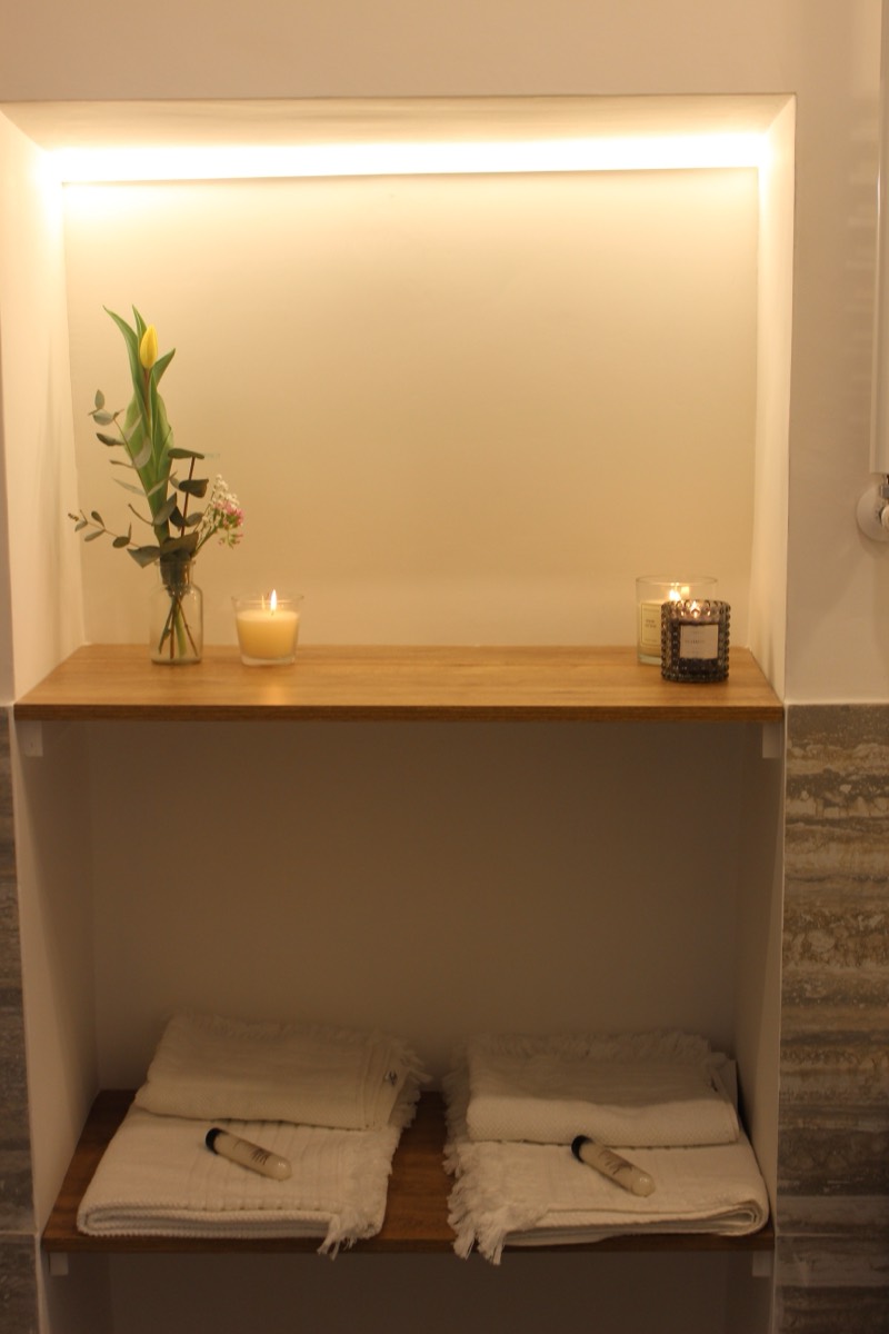 Bathroom shelf with candles, flowers and folded towels